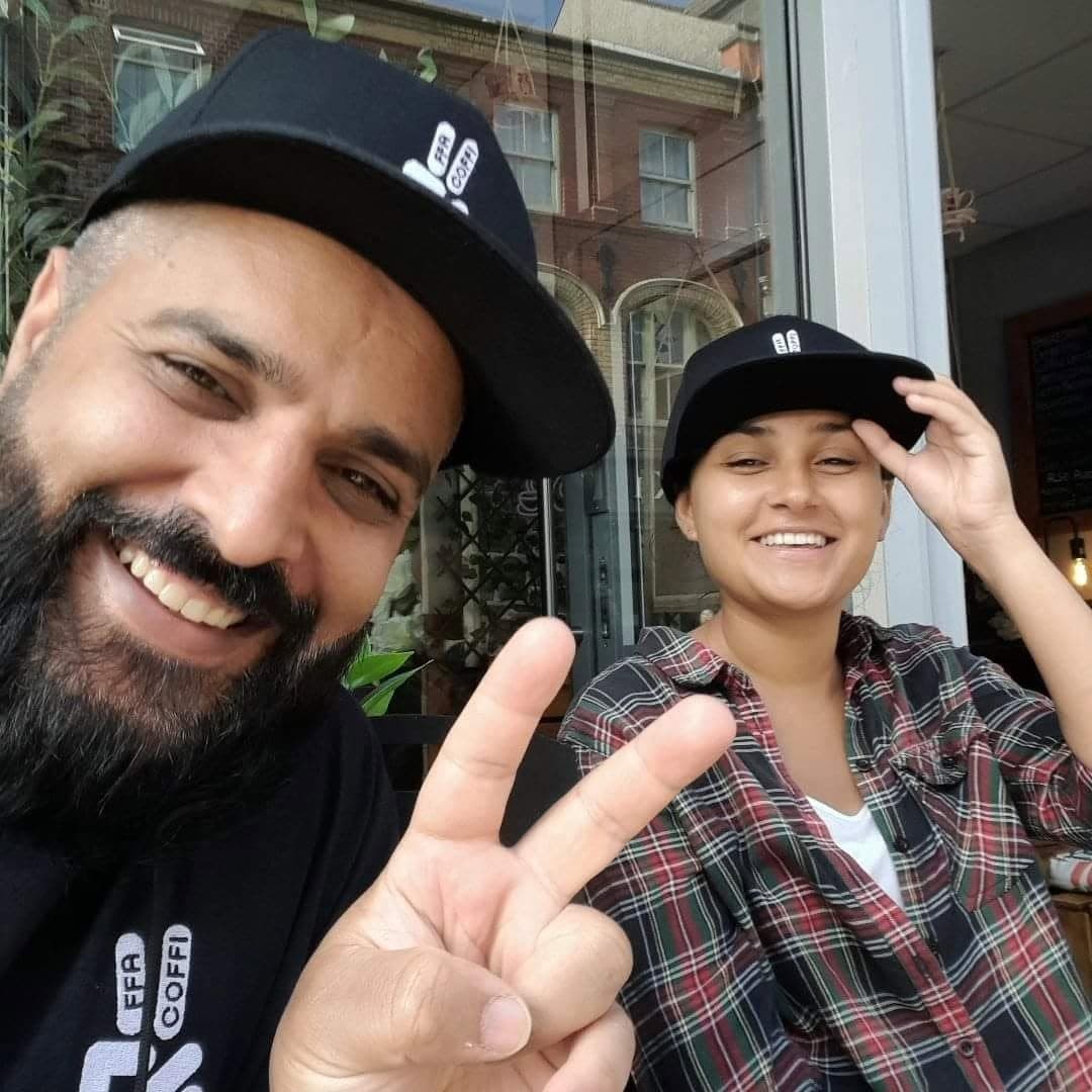 Smiling bearded man and woman in matching black caps, man making a peace sign.