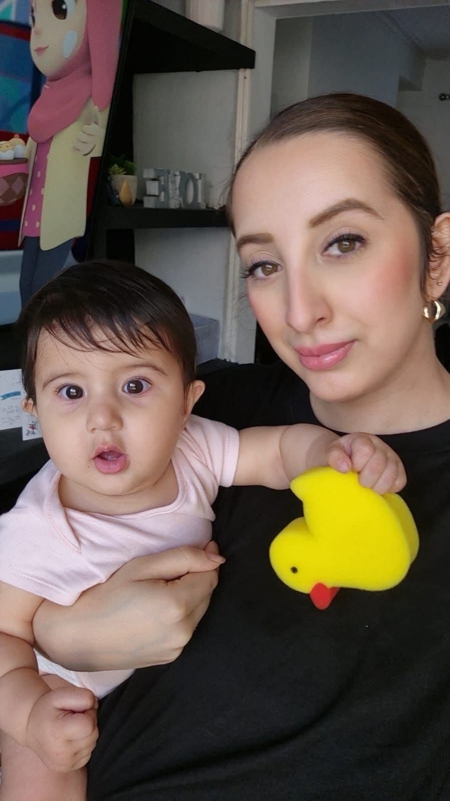 Woman in black holding a baby in pink clutching a yellow duck-shaped sponge.