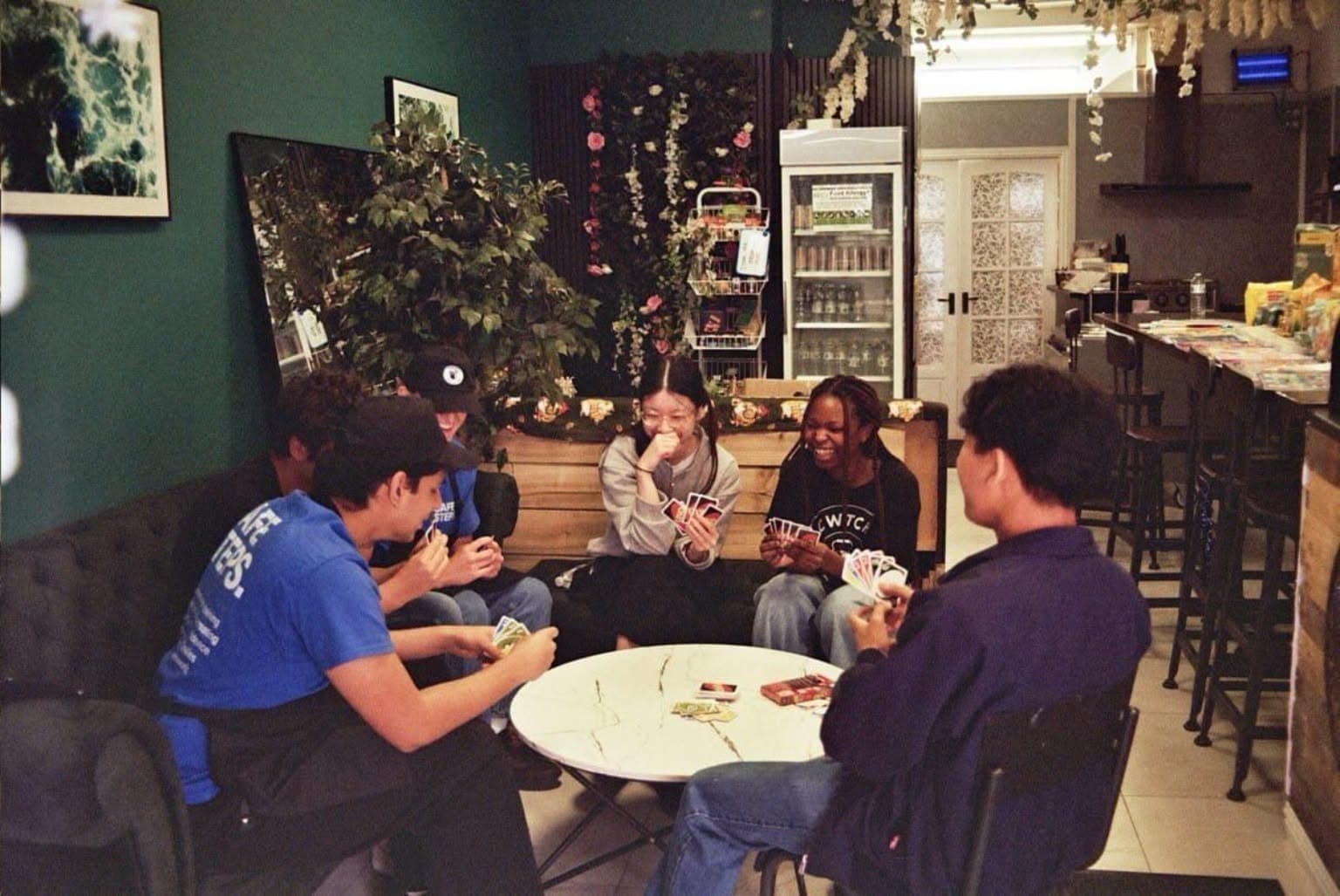 Diverse group of friends laughing while playing a card game around a small white table.